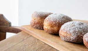 Tradycyjne pączki posypane cukrem pudrem na drewnianej tacy, w kontekście pytania, czy cukrzyk może jeść pączki.